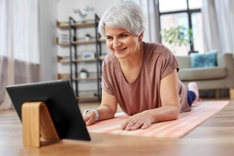 Eine lächelnde ältere Frau mit Tablet-PC-Computer beim Training auf einer Matte zu Hause