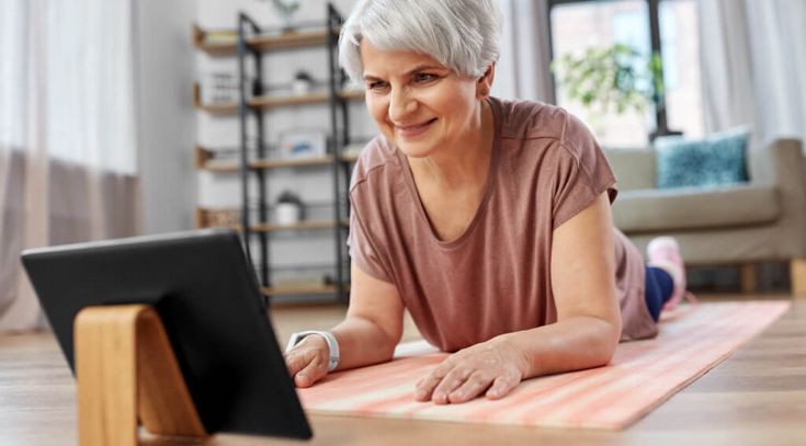 Eine lächelnde ältere Frau mit Tablet-PC-Computer beim Training auf einer Matte zu Hause