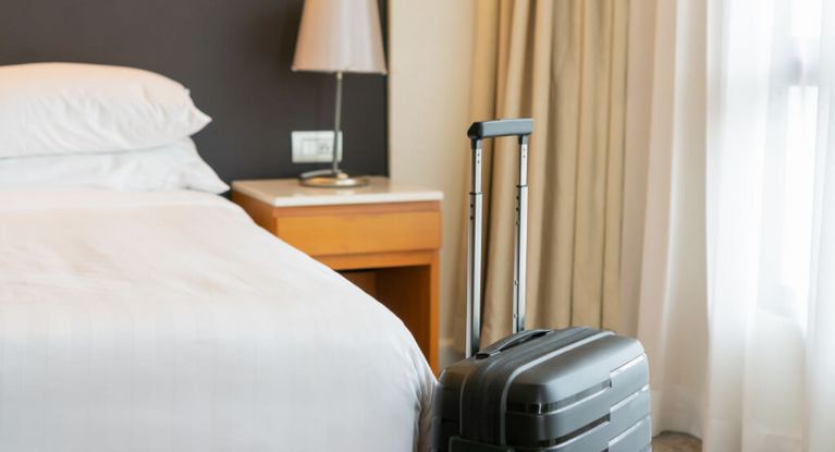ein schwarzer Rollkoffer wartet vor einem frisch gemachten Bett in einem Hotelzimmer